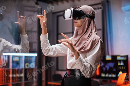 Preview: Muslim business woman in VR glasses standing at office room and gesturing with hands.