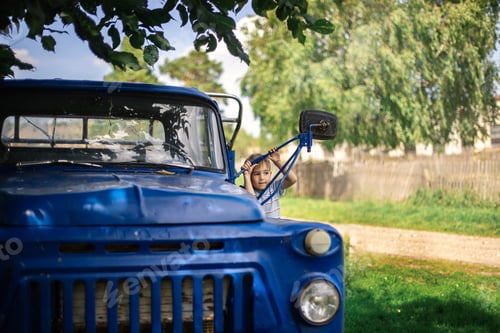 Preview: A child in the countryside plays in a big blue retro car.