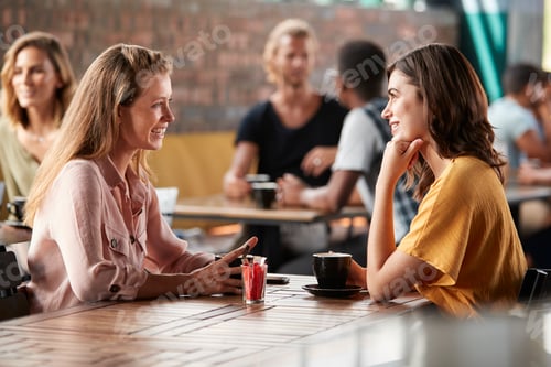 Preview: Two Female Friends Sitting At Table In Coffee Shop And Talking