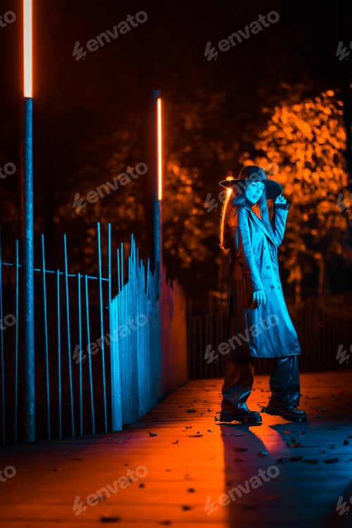 Preview: Caucasian brunette girl with hat at night in a park illuminated with blue light