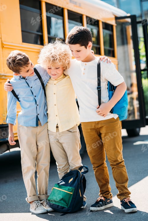 Preview: happy little schoolboys spending time together in front of school bus