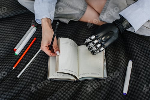 Preview: Cropped image of woman sitting on bed opens diary using biomechanical hand.