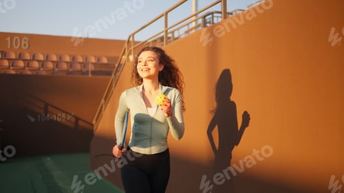 Preview: Young adult girl with curly hair running on the court with pickleball paddle and ball in the hands