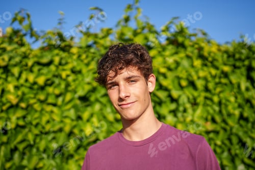 Preview: Cheerful male leaning against verdant ivy wall, exuding joy with bright smile and relaxed demeanor