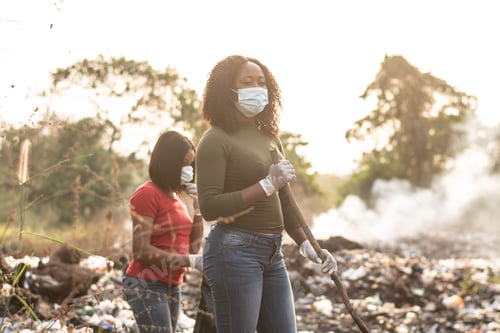Preview: Nigerian women cleaning up together a dump site with trees and smoke in the background in Nigeria