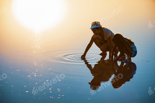Preview: Two girls on a beautiful transparent lake are looking for something in a shiny surface
