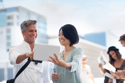 Preview: Group of happy casual businesspeople sharing tablet on urban square