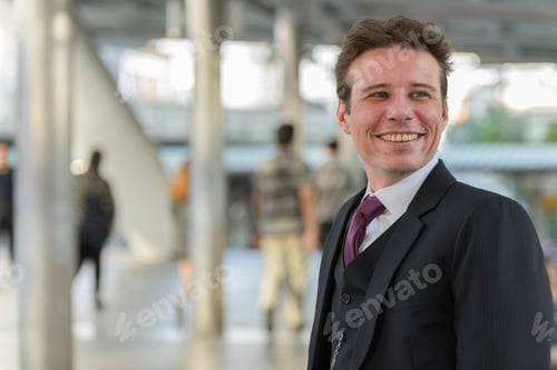 Preview: Happy businessman smiling and thinking outdoors in city