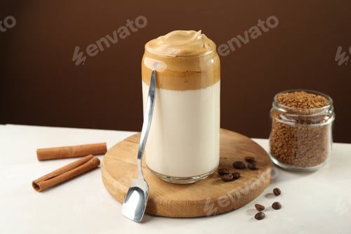 Preview: Delicious dalgona coffee in glass, beans, granules and cinnamon on white table