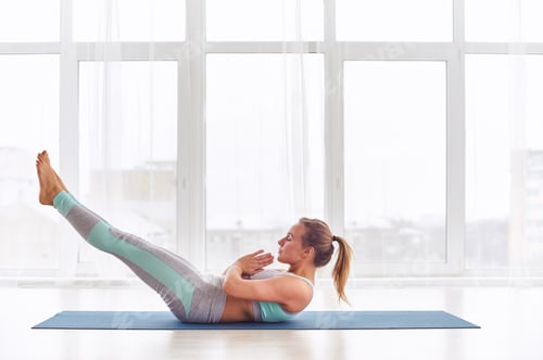 Young woman practicing yoga asana Ardha Navasana exercise at the yoga studio