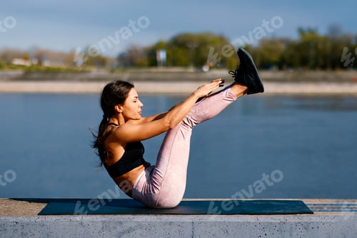 Preview: Sportswoman practicing boat pose exercise near the river in the urban area