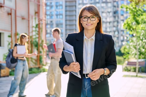 Preview: Portrait woman teacher looking at camera, outdoor, group of students background