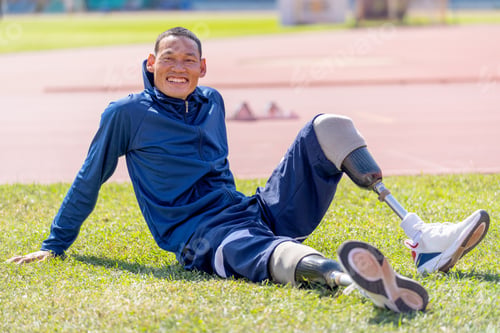 Preview: Close up sport man athlete with a prosthesis on his leg sit on grass field near track look at camera