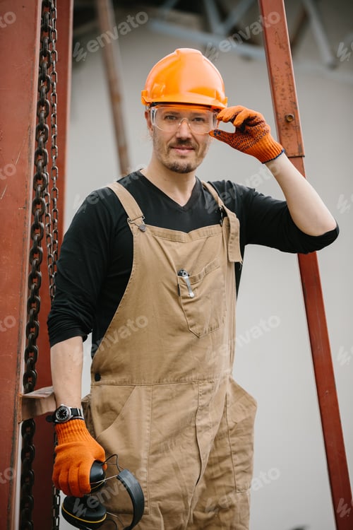 Preview: A construction worker in a protective helmet and glasses at the construction site of a grain silo.