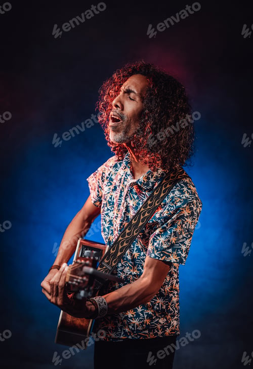 Preview: Hispanic musician emotionally singing and playing guitar on a dark illuminated by blue and red light