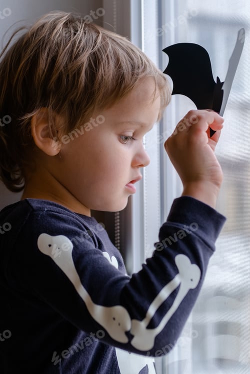 Preview: A brooding boy in a skeleton costume and a witch hat for Halloween is sitting at the window