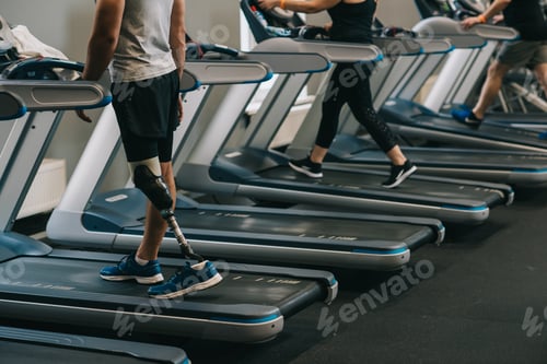 Preview: cropped shot of man with artificial leg running on treadmills at gym with other people