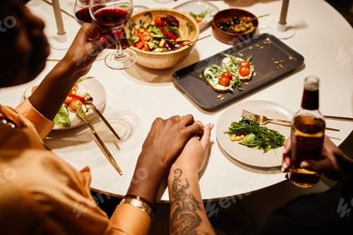 Preview: Hands of two young lesbian women with alcoholic drinks sitting by served table