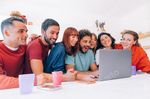 Preview: group of seven happy friends watching online streaming together on laptop in the kitchen of a house