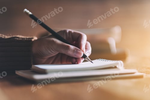 Preview: Closeup image of a woman writing on blank notebook on wooden table