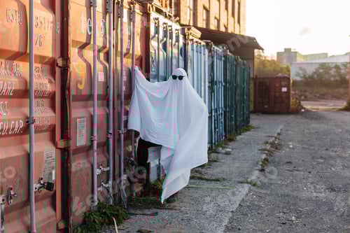 Preview: A girl in a white sheet and sunglasses dressed as a ghost on Halloween walks by the containers