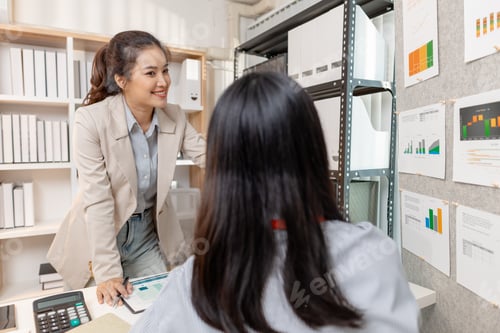Preview: Two Asian businesswomen discussing company strategy together in a modern office