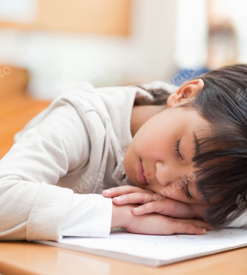 Preview: Asian child girl sleeping at desk in study area with colored pencil drawings on wooden surface