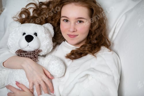 Preview: A young girl in a white suit hugs a white teddy bear and smiles