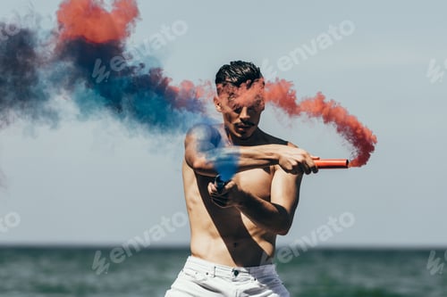 Preview: handsome shirtless man with red and blue smoke sticks in front of ocean view