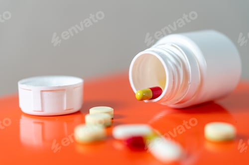 Preview: Pill bottle with spilled pills and capsules on orange surface