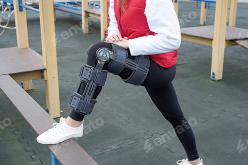 Preview: Woman wearing knee brace or orthosis after leg surgery, walking in the park