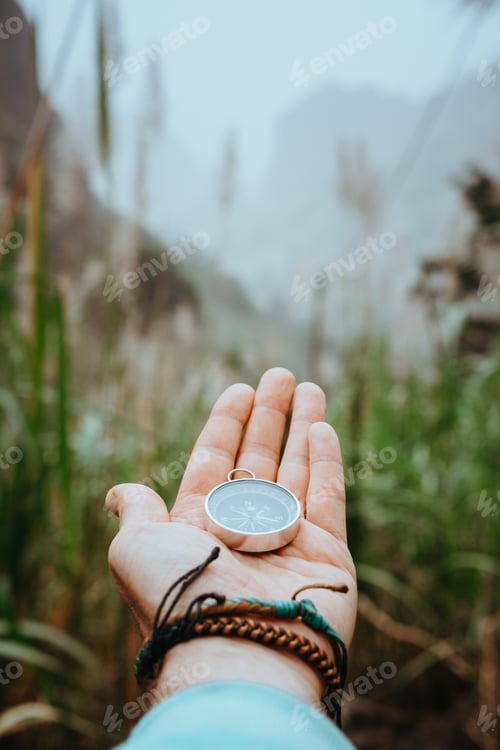 Preview: Man arm with compass on the palm stretched out to determine position in mountains on cloudy day