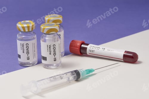 Preview: Closeup of a syringe needle with the COVID-19 test and vaccine ampoules on the table