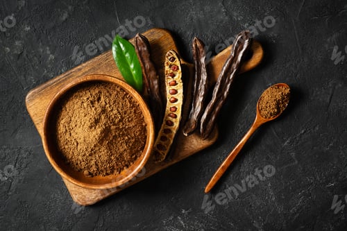 Preview: Carob bean and powder on board flat lay on black background