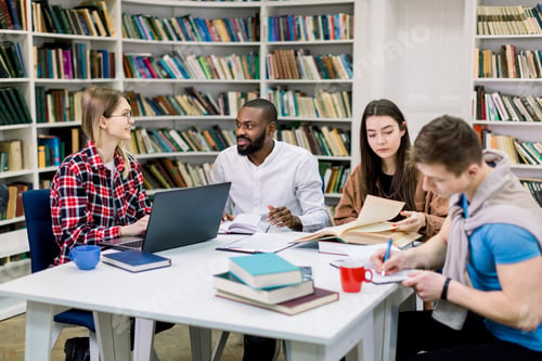 Preview: Four multiracial happy students sitting at table in library while learning and working on a laptop