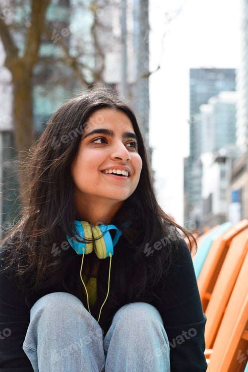 Preview: Closeup portrait of happy young girl sitting on city street smiling