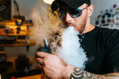 Preview: Brutal bearded man in sunglasses smoke an electronic cigarette and releases clouds of vapor at the