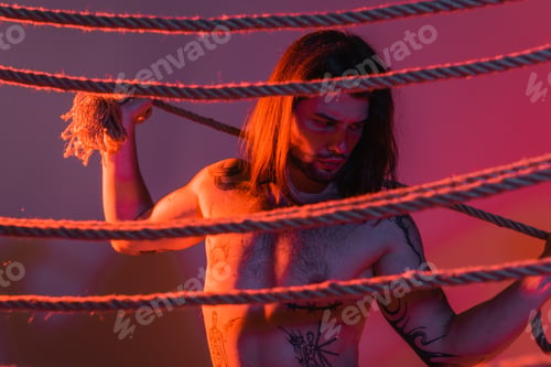 Preview: Sexy tattooed model holding rope on purple background with light