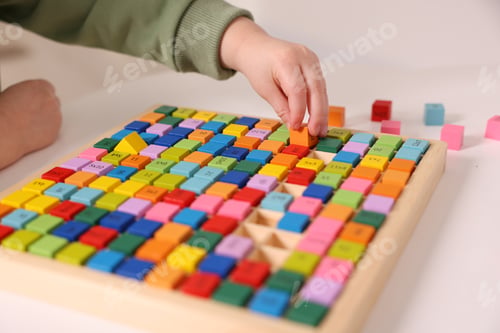 Preview: Motor skills development. Little boy playing with Times table tray indoors, closeup