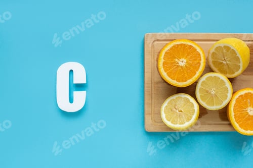 Preview: top view of ripe cut lemon and orange on wooden cutting board near letter C on blue background