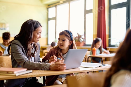 Preview: Happy teacher and schoolgirl using laptop during computer class in the classroom.