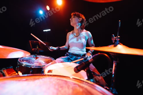Preview: Female drummer performing energetically on stage with colorful lighting