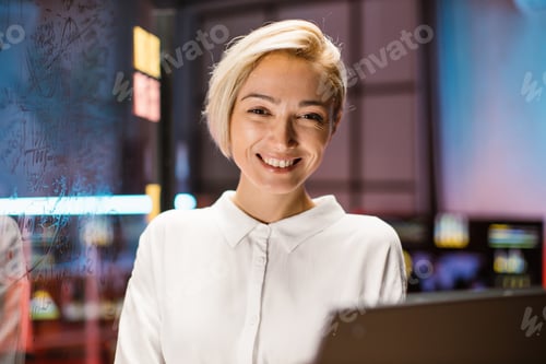 Preview: Caucasian business woman in white shirt, posing on camera, while standing in modern dark office