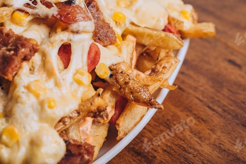 Preview: Closeup shot of a dish with french fries, sausages topped with cheese and corn on a wooden table.