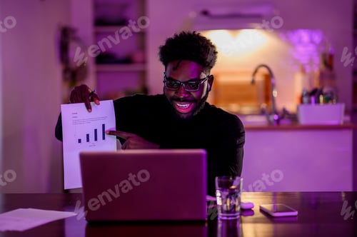 Preview: A happy interracial data analyst is showing a chart at the laptop while having an online meeting.