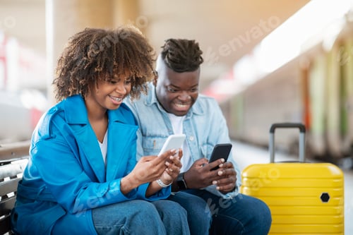 Preview: Black Couple Playing Games On Smartphones While Waiting Train At Railway Station