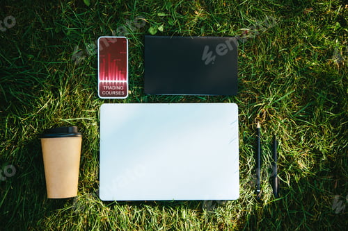 Preview: top view of smartphone with trading courses appliance and coffee in paper cup on green grass in park