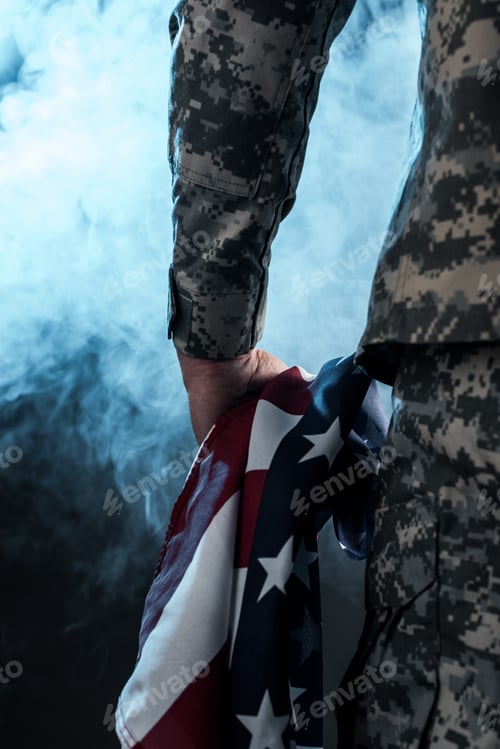 Preview: cropped view of soldier holding american flag on black with smoke