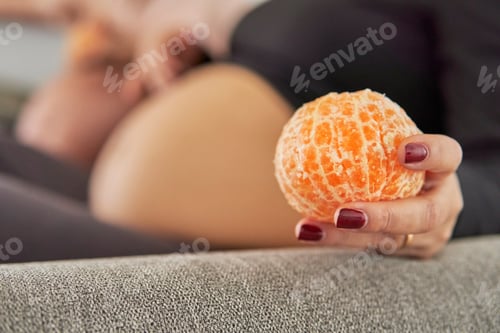 Preview: Healthy eating on the pregnancy. Peeled tangerine on the hand of a pregnant women at home