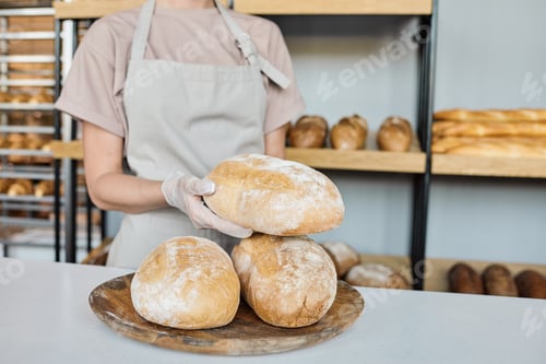 Preview: Young gloved baker holding fresh baked loaf of bread